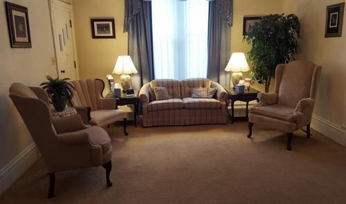 Living room with sofa, armchairs, lamps, and a large plant near a window.