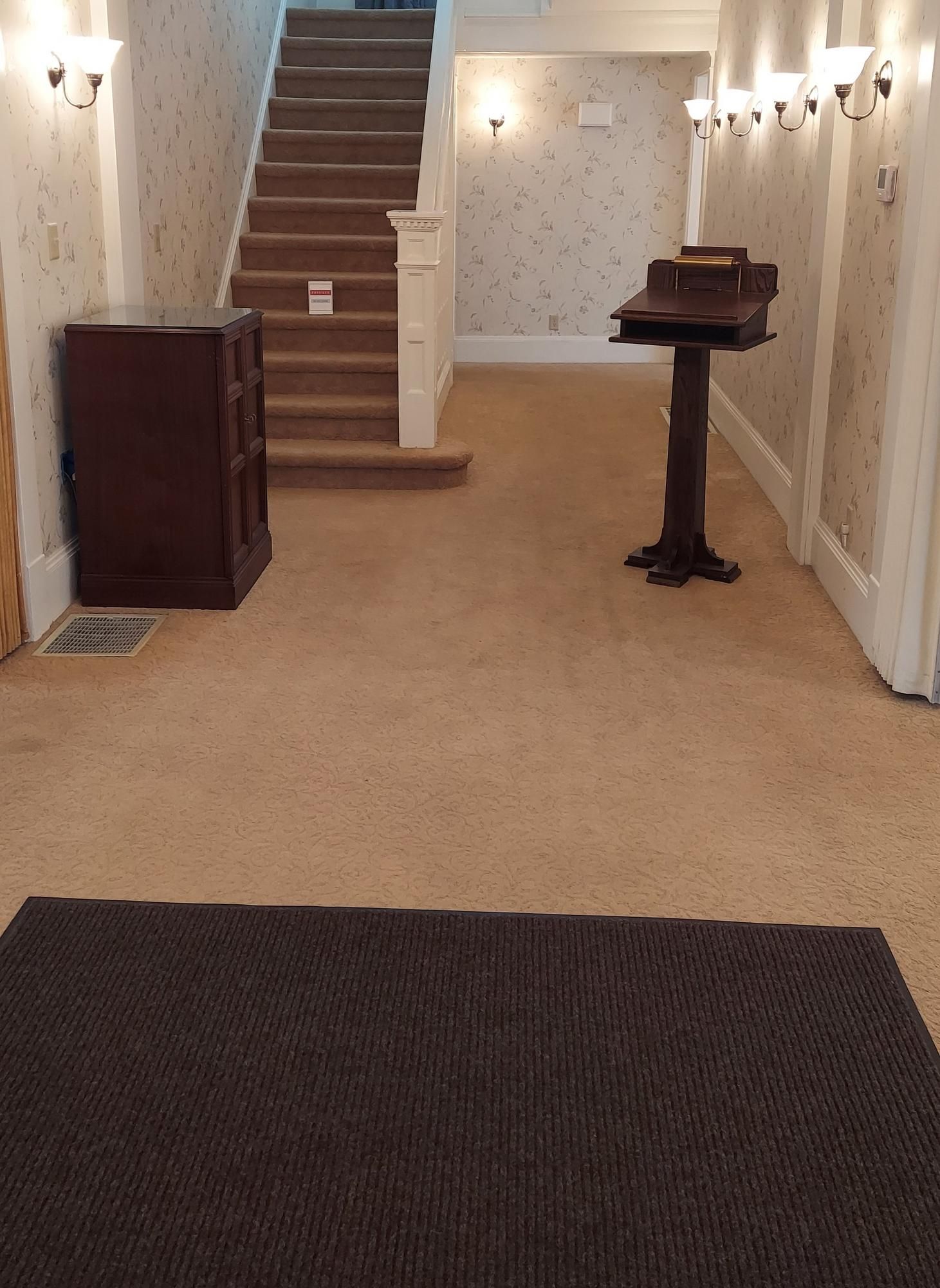 An interior hallway with stairs and a podium. Beige carpet, brown wood furniture, and off-white walls.