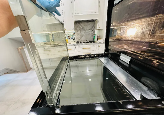A person removing the glass door of a dirty oven for cleaning.