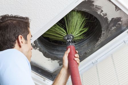 Man cleaning air vent with a brush. Inside the vent, green brush is visible.
