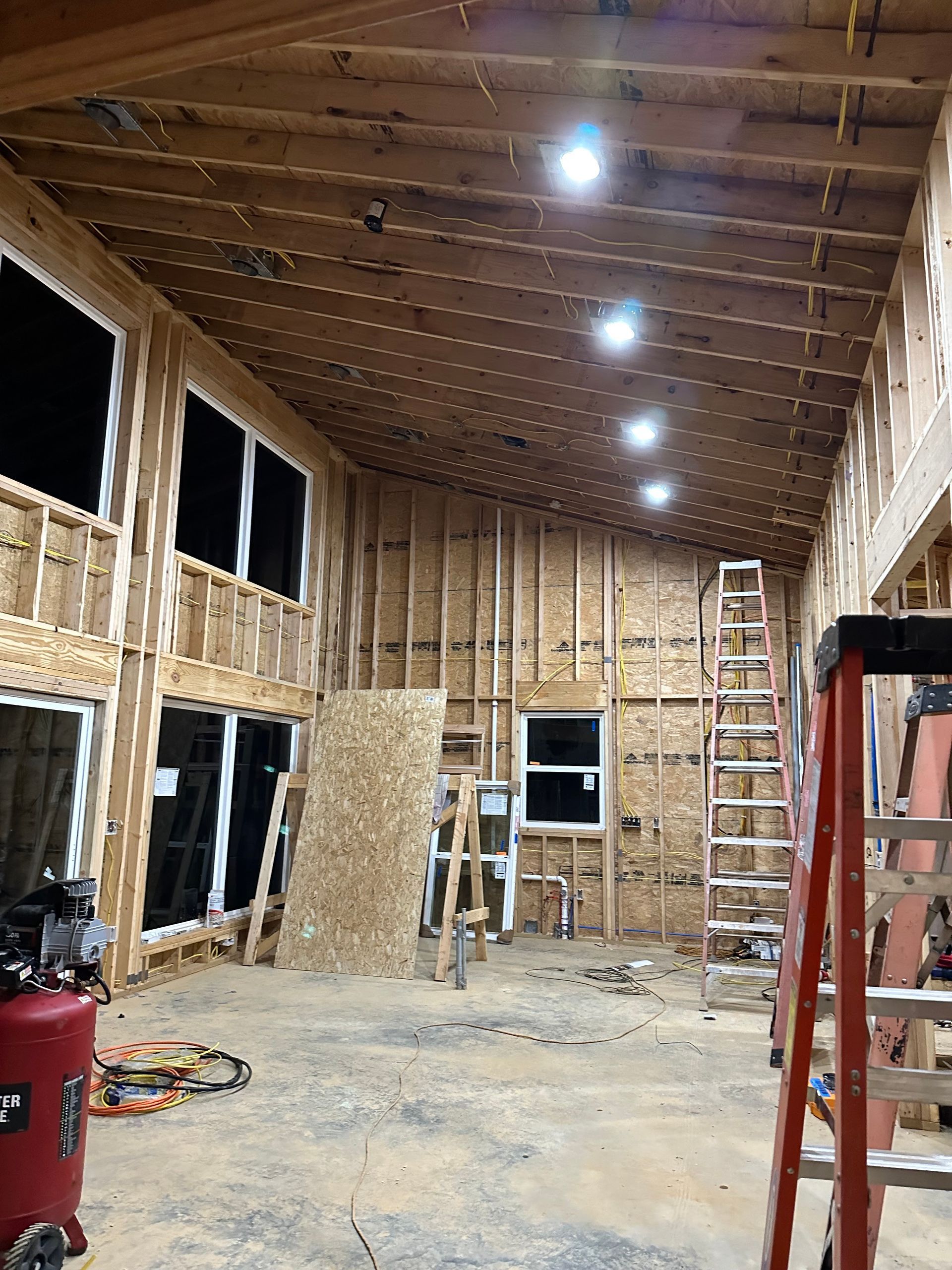 A large room under construction with a ladder and a vacuum cleaner.