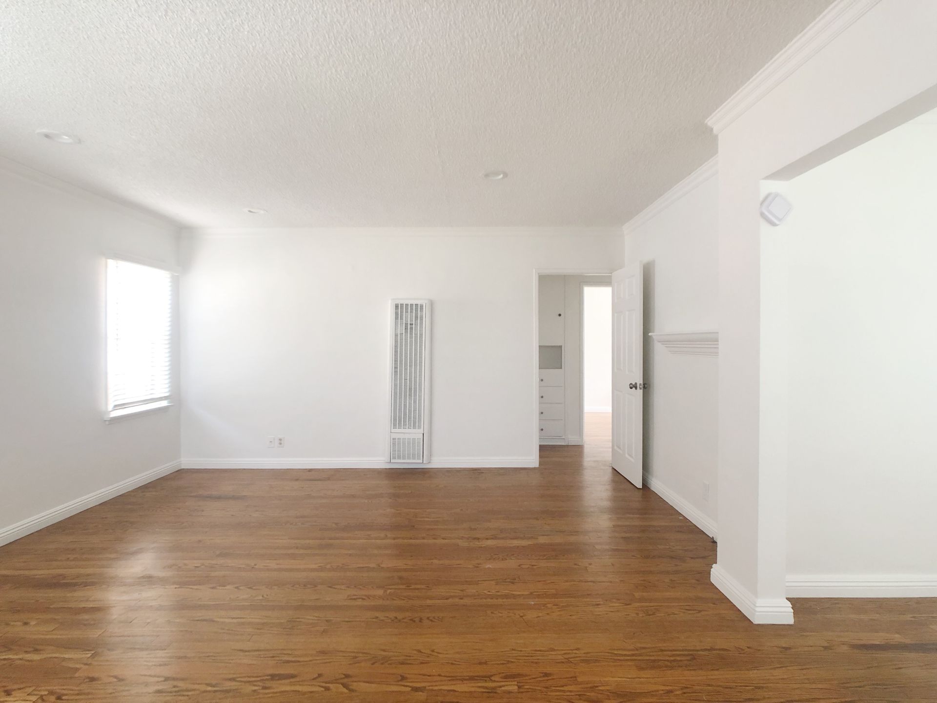 An empty living room with hardwood floors and white walls.