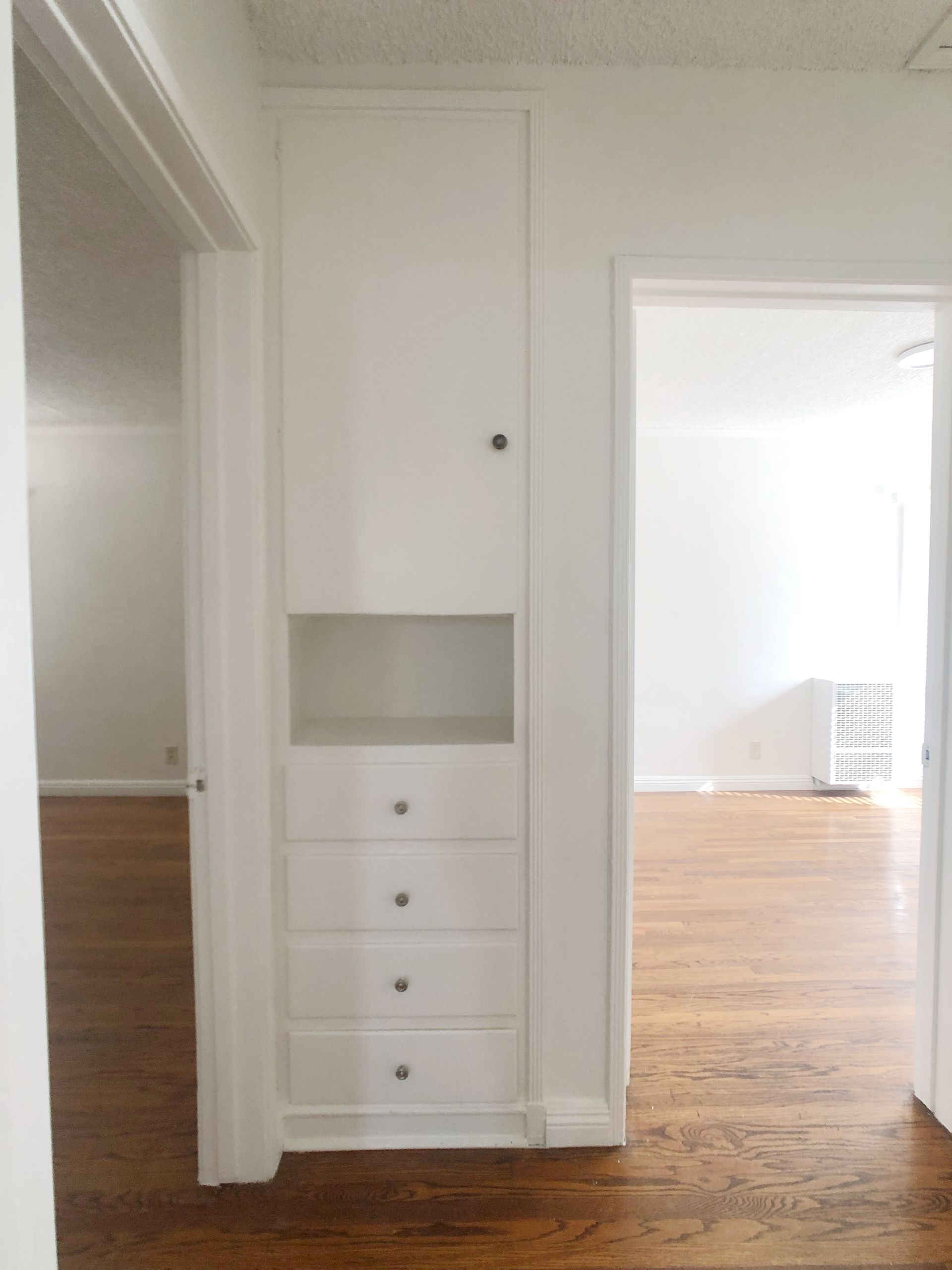 An empty hallway with a white cabinet and drawers