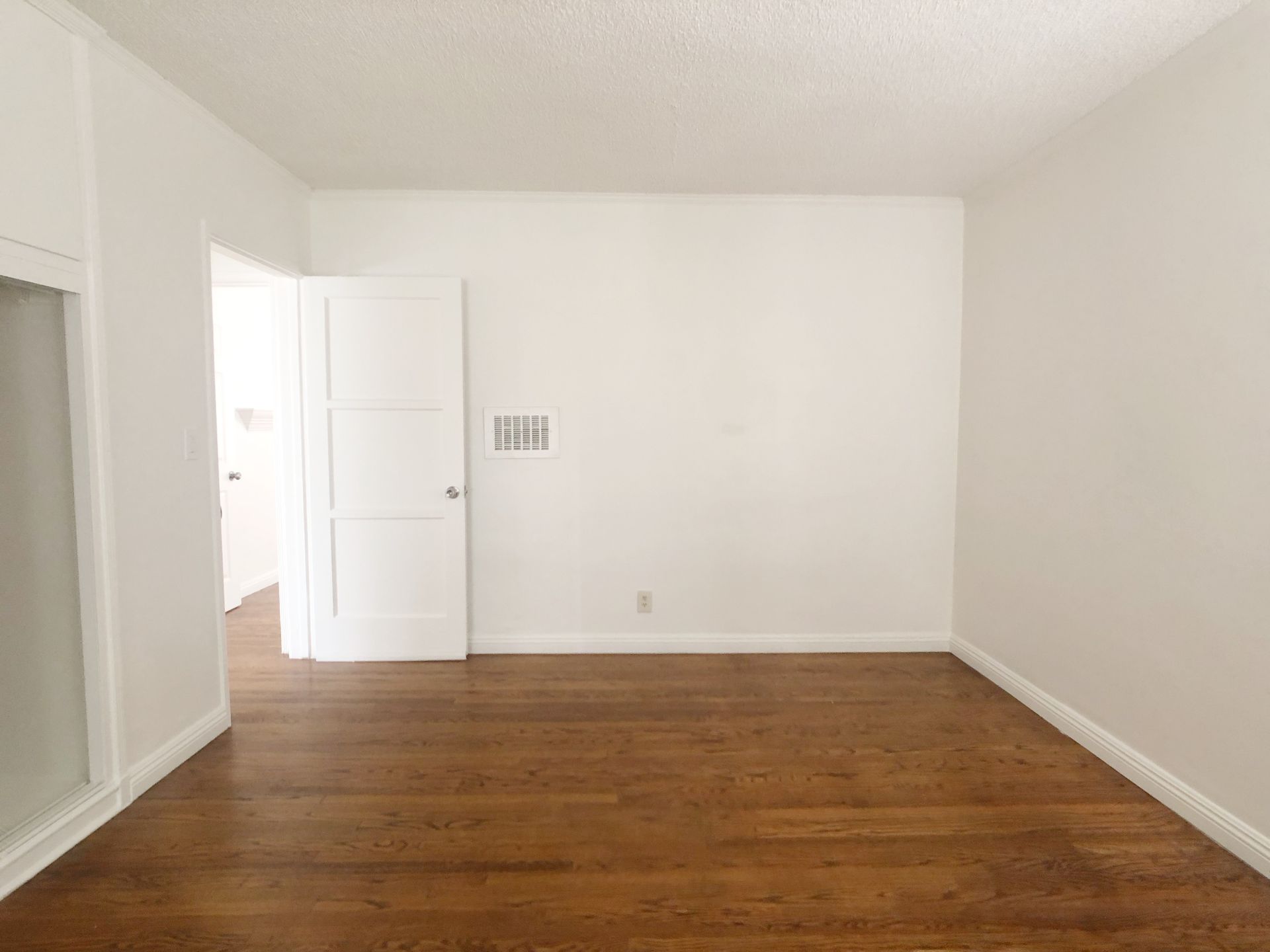 An empty living room with hardwood floors and white walls.