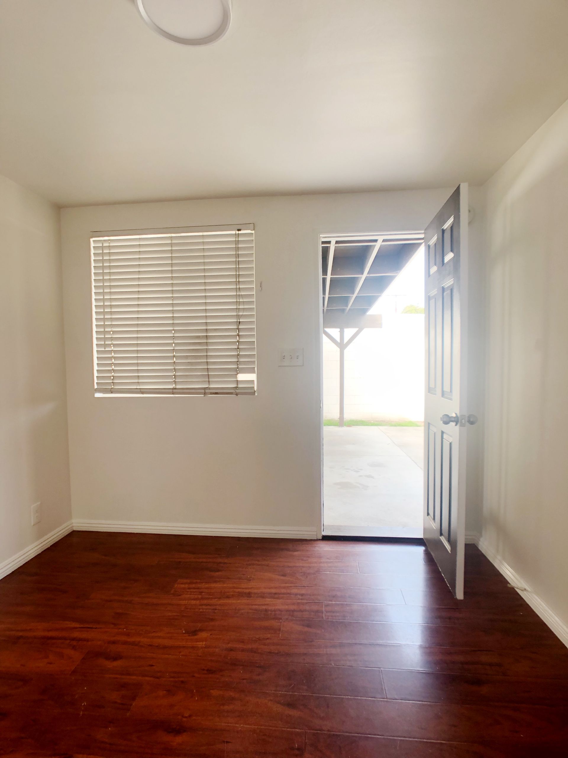 An empty room with hardwood floors and a window with blinds.