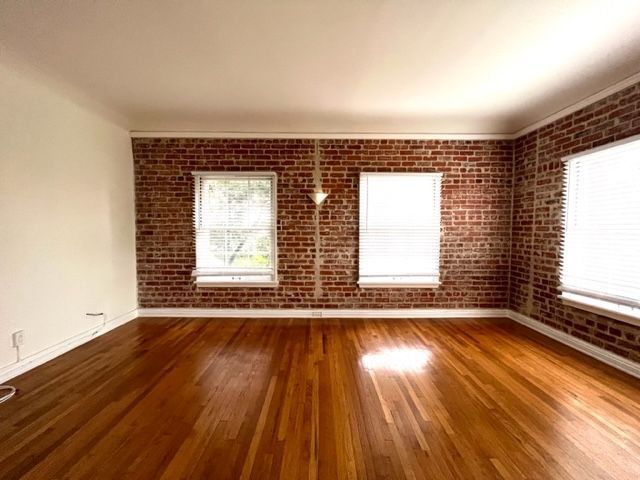 An empty living room with hardwood floors and brick walls.