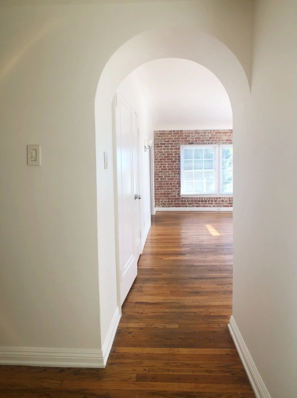 A hallway leading to a living room with a brick wall