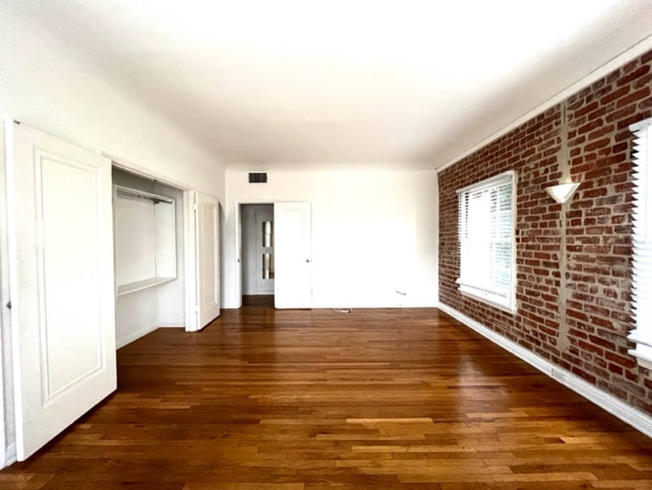 An empty living room with hardwood floors and brick walls