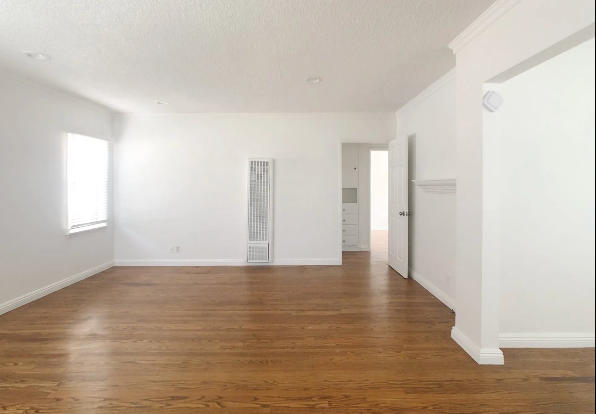 An empty living room with hardwood floors and white walls