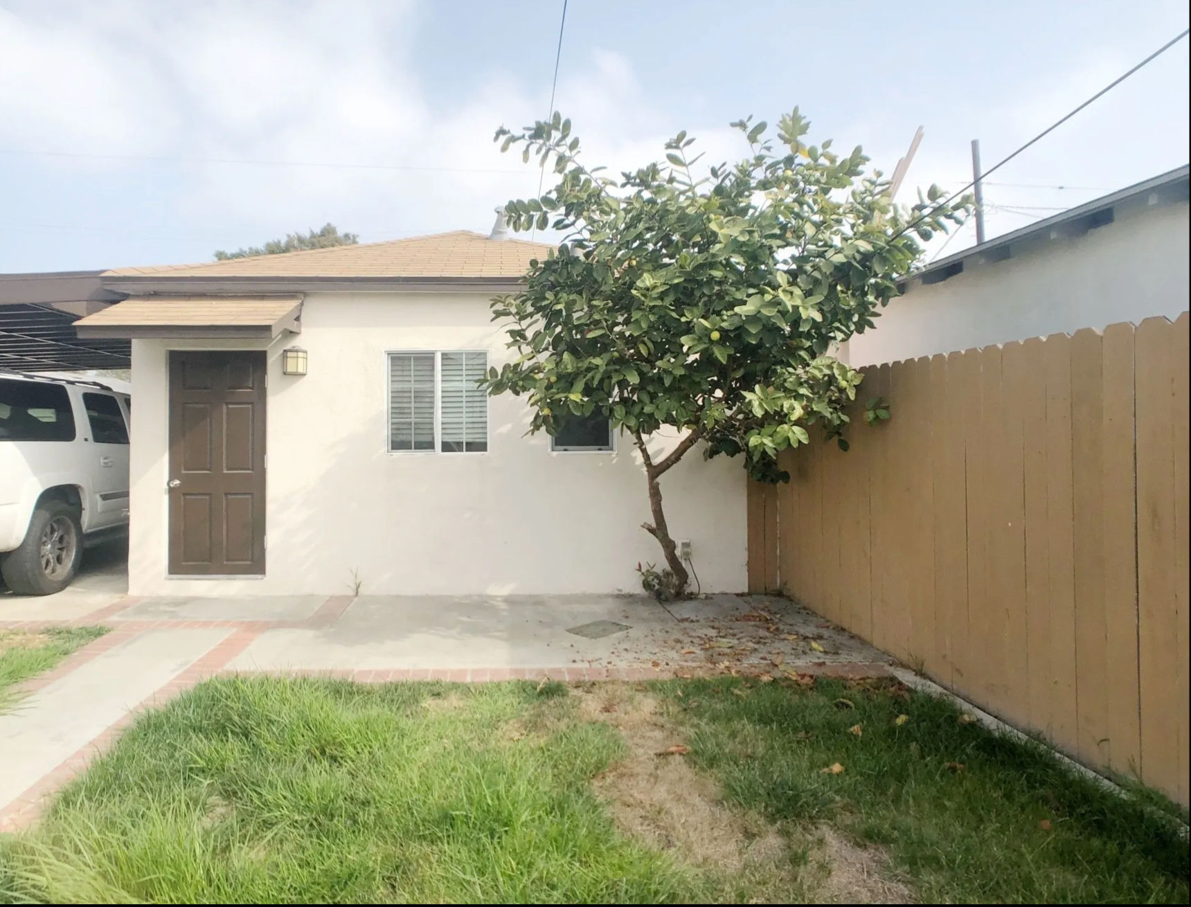 A white house with a tree in front of it and a car parked in front of it.