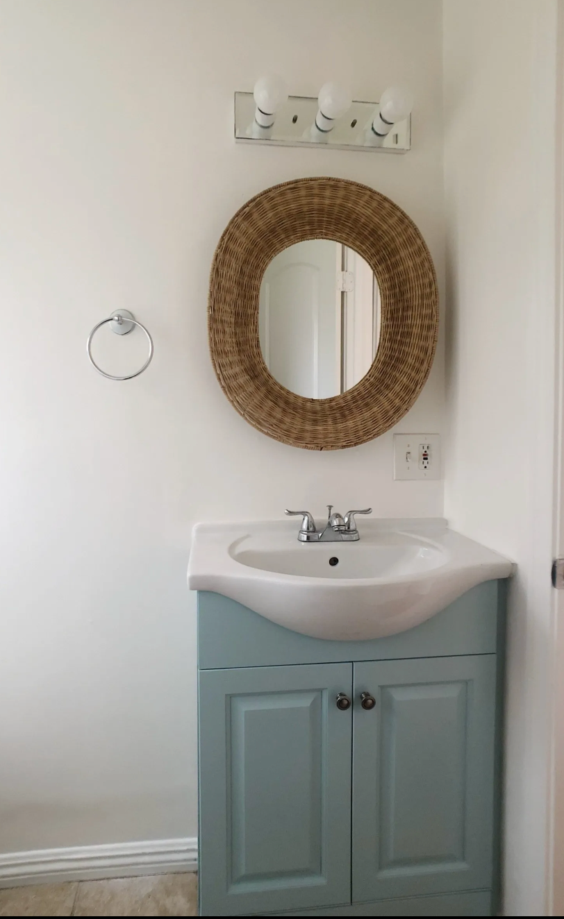 A bathroom sink with a wicker mirror above it