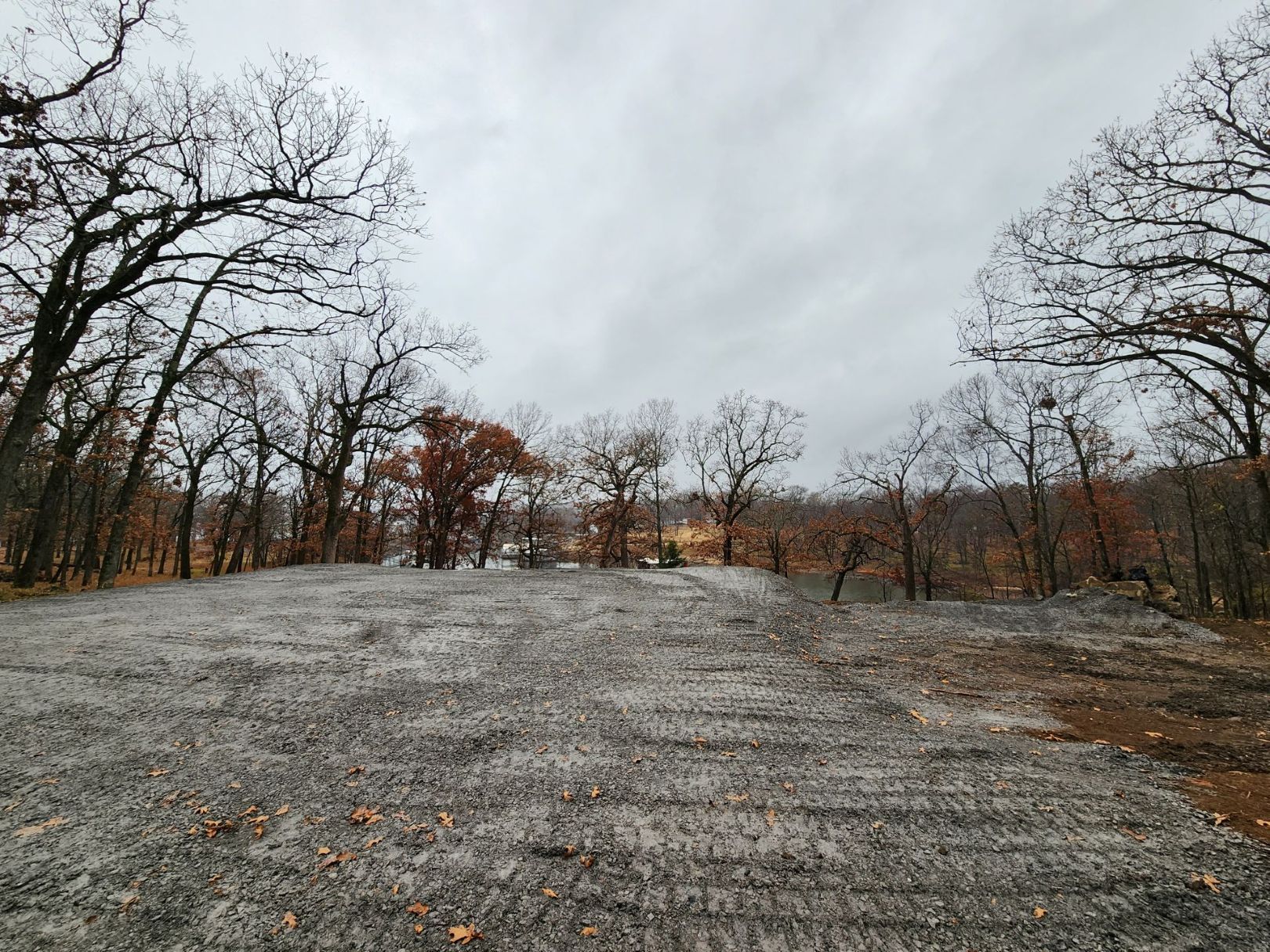 Gray gravel area surrounded by bare trees under an overcast sky.