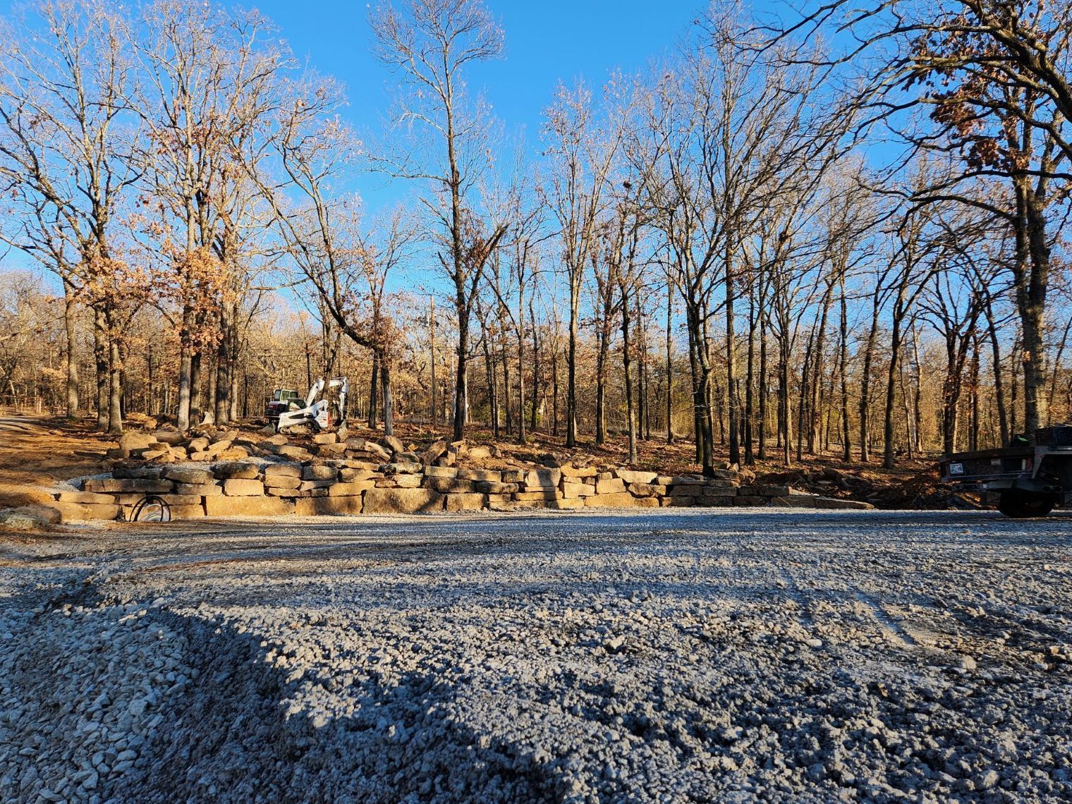 Gravel driveway with a construction site in the background, surrounded by bare trees under a clear blue sky.