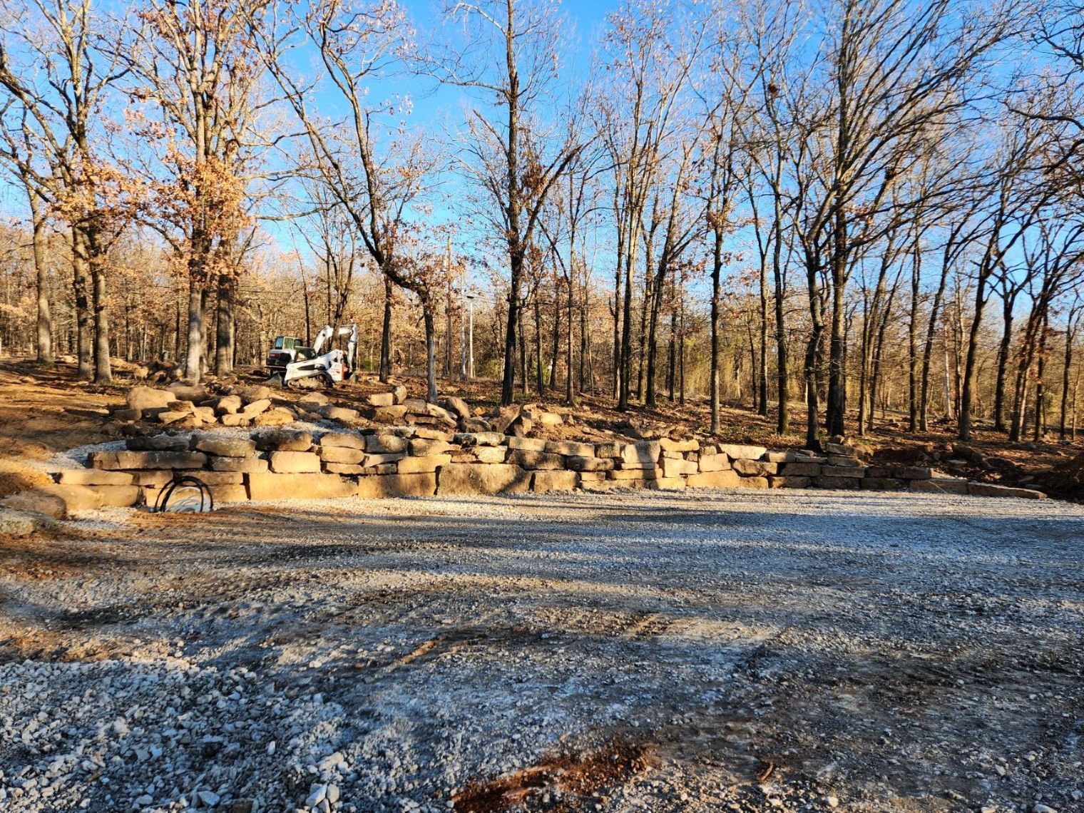 Gravel driveway in front of a stone retaining wall and bare trees.