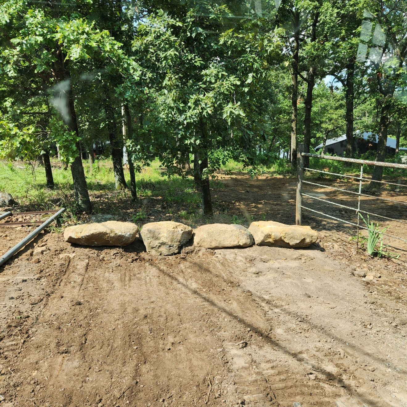 Dirt path with four large rocks blocking access, trees in background.