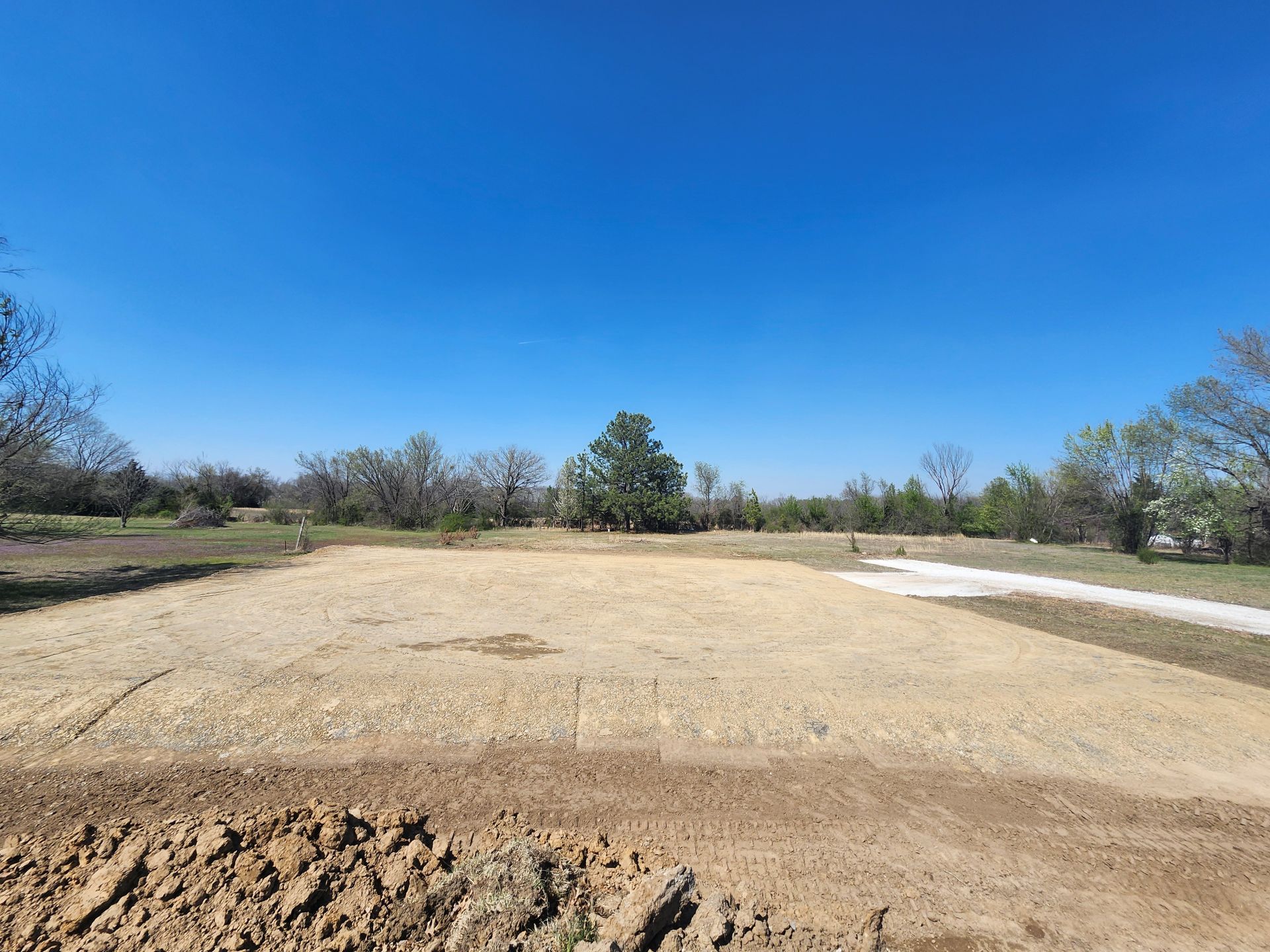 Cleared, level dirt area with trees under a blue sky.