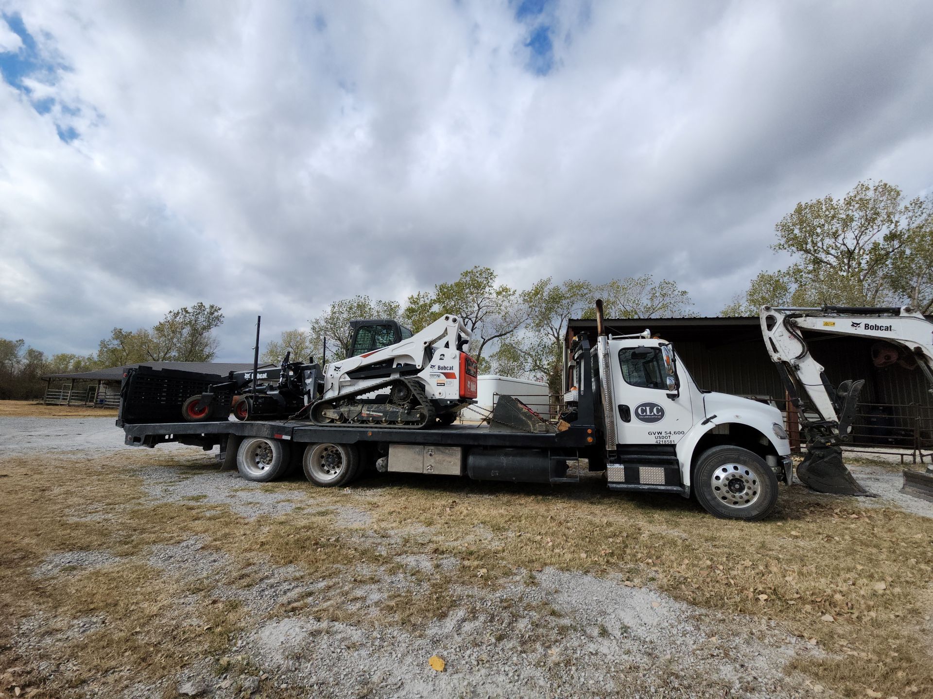 White truck hauling construction equipment under a cloudy sky.