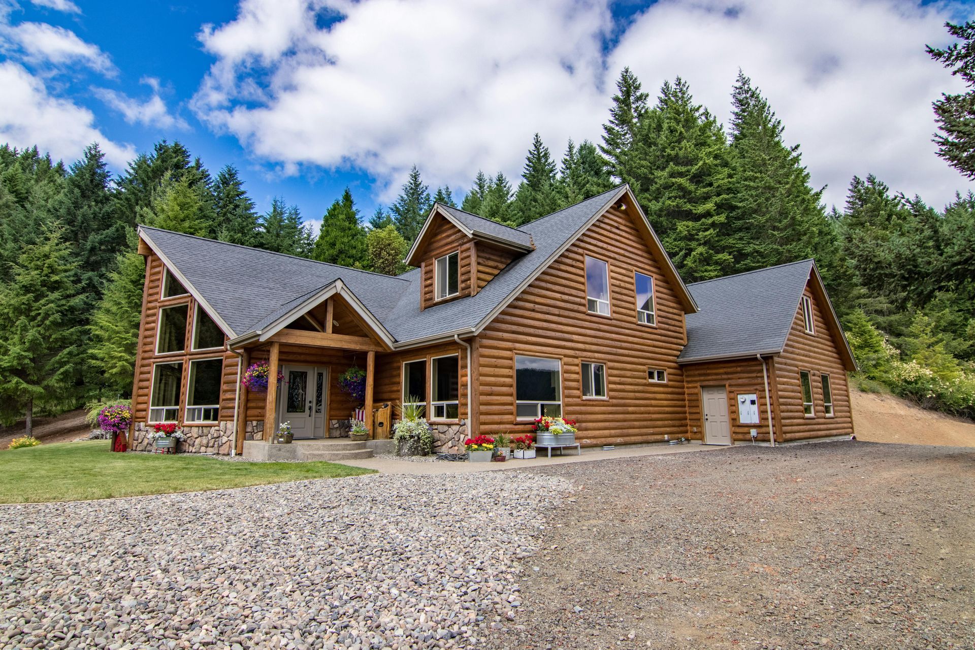 Log cabin home with wooden siding, surrounded by trees and a gravel driveway.
