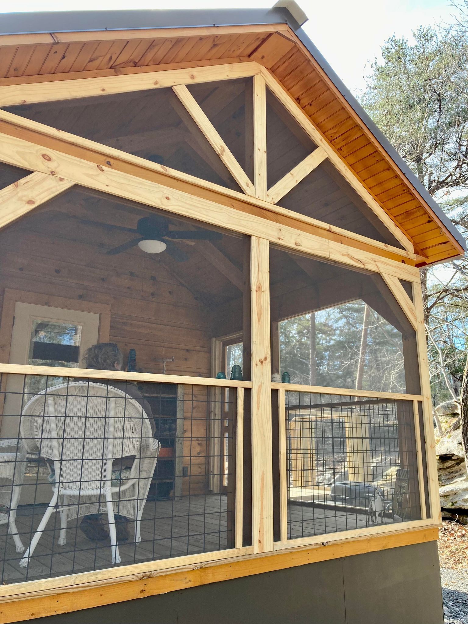 A screened in porch with a table and chairs and a ceiling fan.