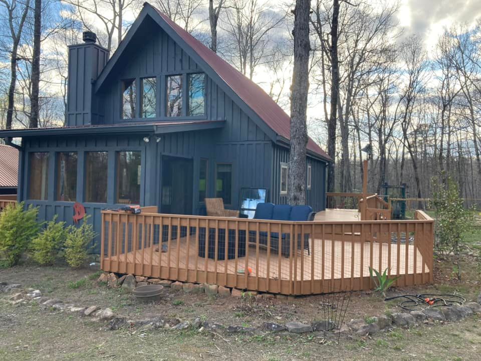 A black house with a wooden deck in front of it surrounded by trees.