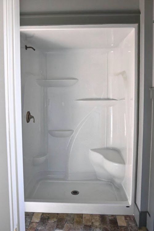 A white shower stall with a shower head and shelves in a bathroom.