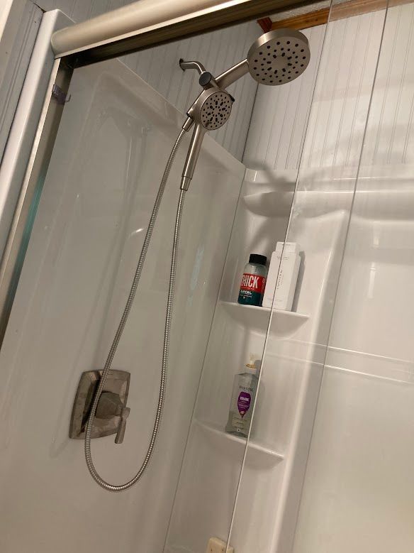 A shower head is hanging from a shower door in a bathroom.