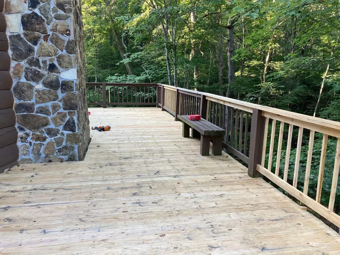 A wooden deck with a bench and railing in the woods.