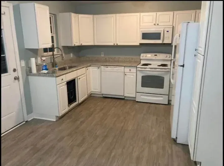 A kitchen with white cabinets , a stove , a refrigerator , and a sink.