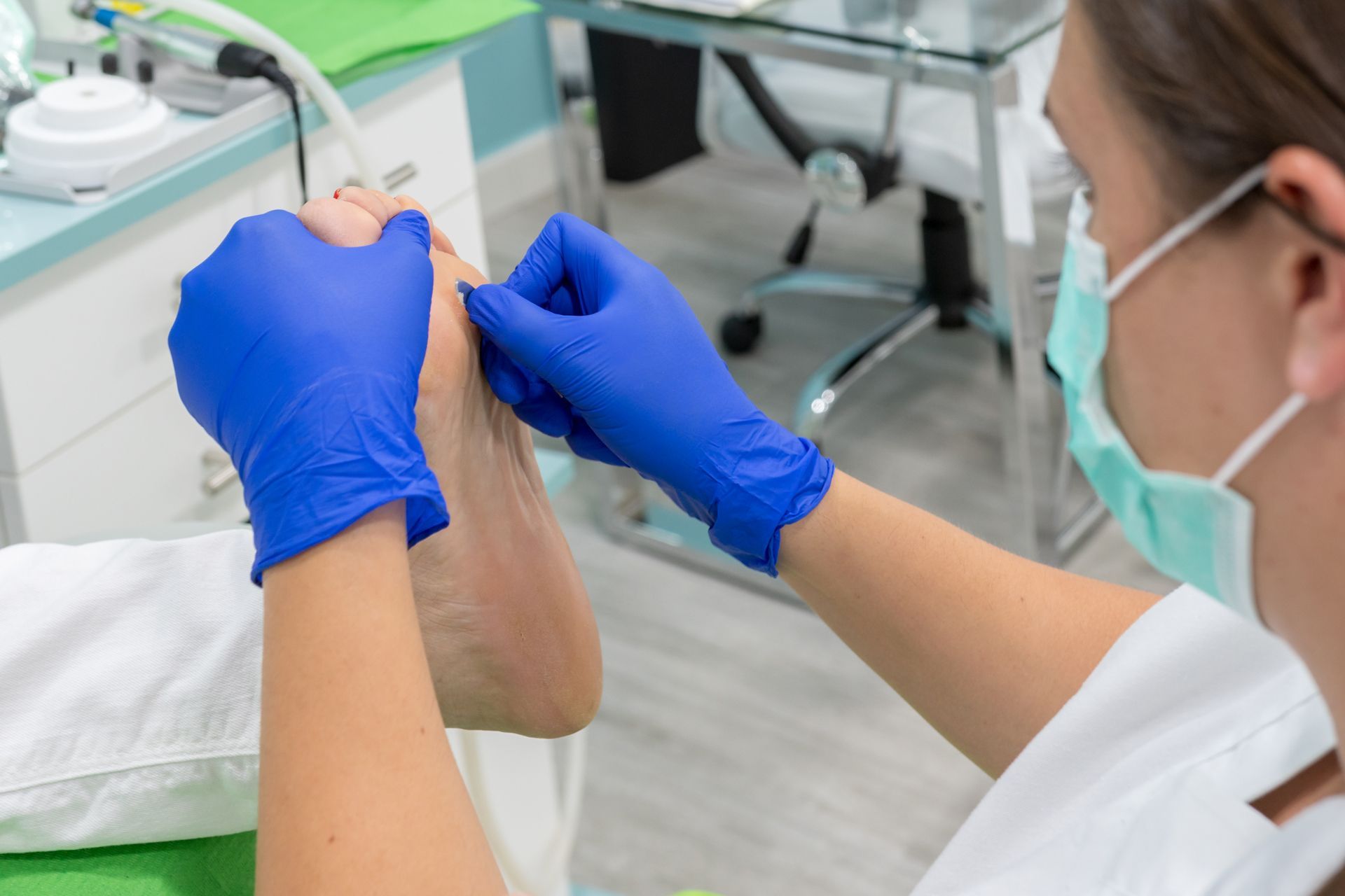 Woman Wearing a Mask and Blue Gloves Is Examining a Patient's Foot
