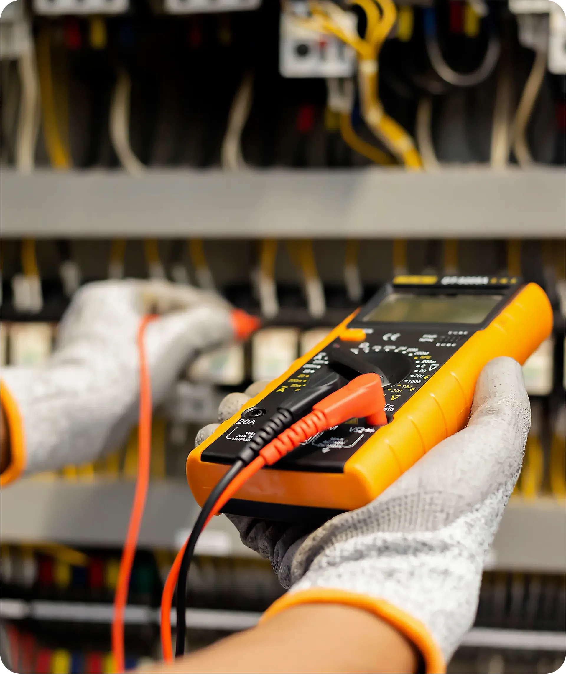 Electrician testing wires with a multimeter in a control panel, wearing gloves.