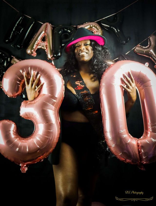 Woman posing with pink “30” balloons and a matching pink hat at a birthday celebration