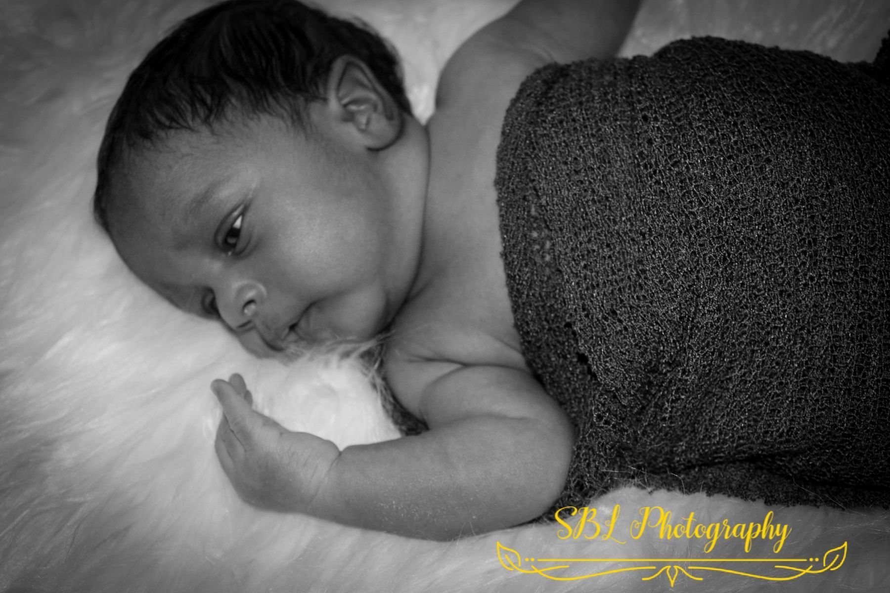 Sleeping baby lying on a white blanket, wrapped in a dark cloth