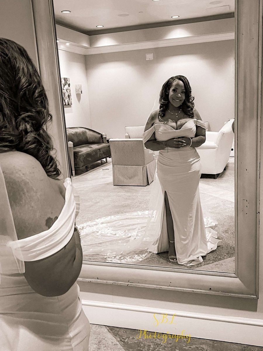 Woman in a white dress posing in a mirror in a softly lit room.