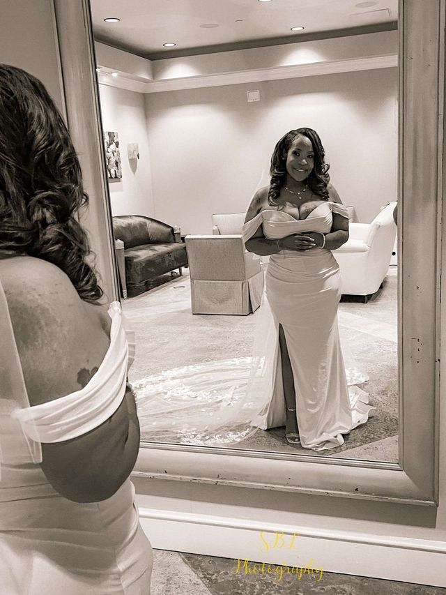 Woman in a white dress posing in a mirror in a softly lit room.