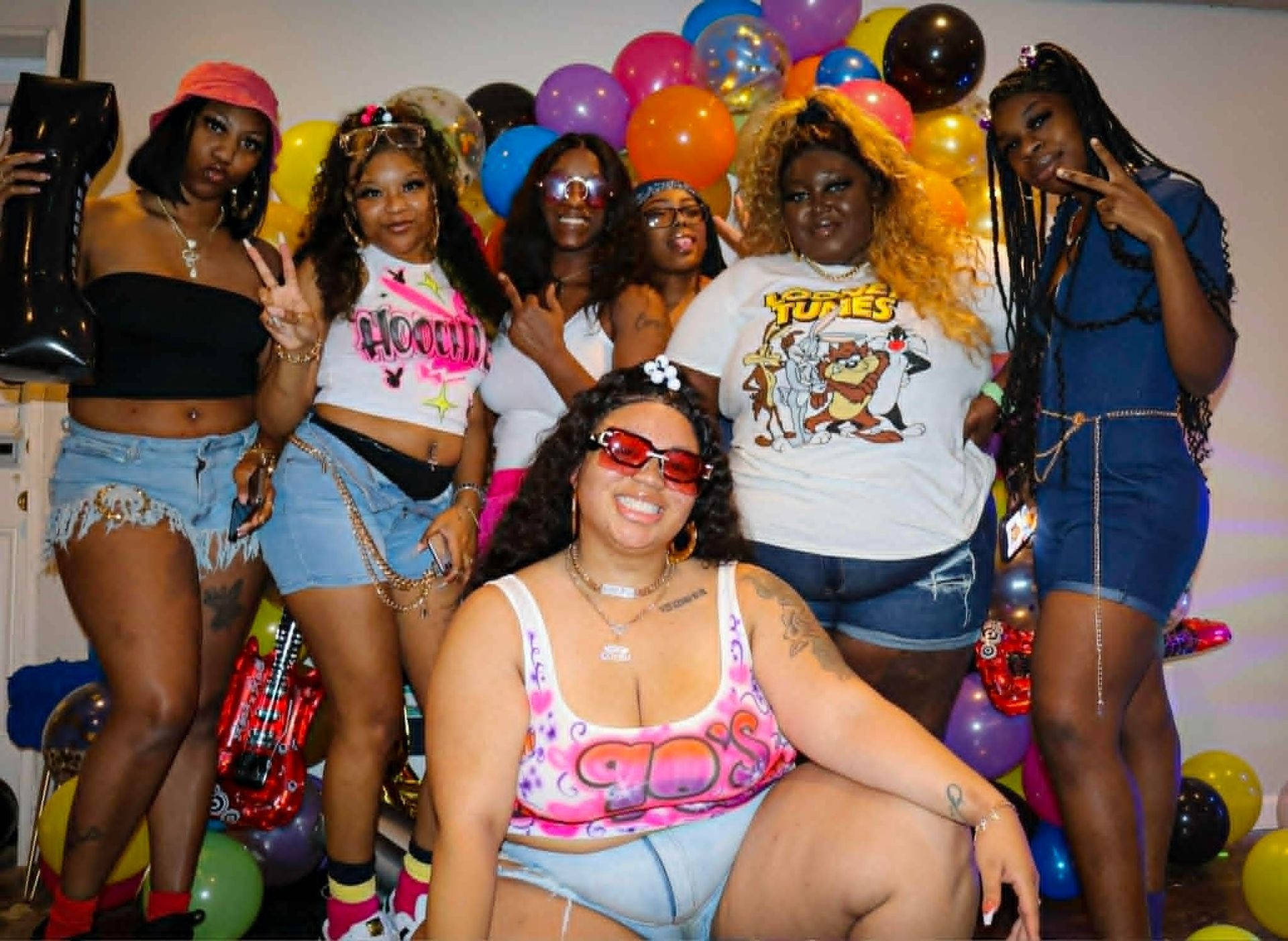 Group posing in front of colorful balloons, smiling and dressed in bright party outfits