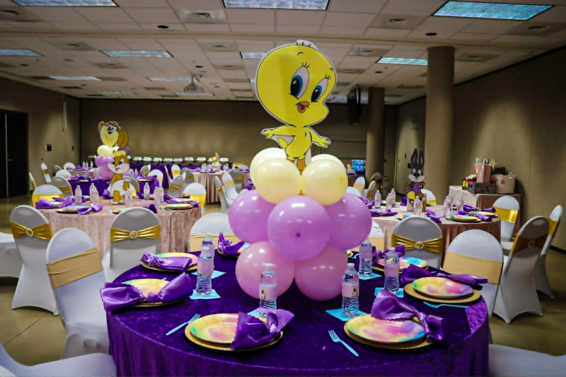 Tweety Bird-themed party table with purple and yellow decorations in a banquet hall
