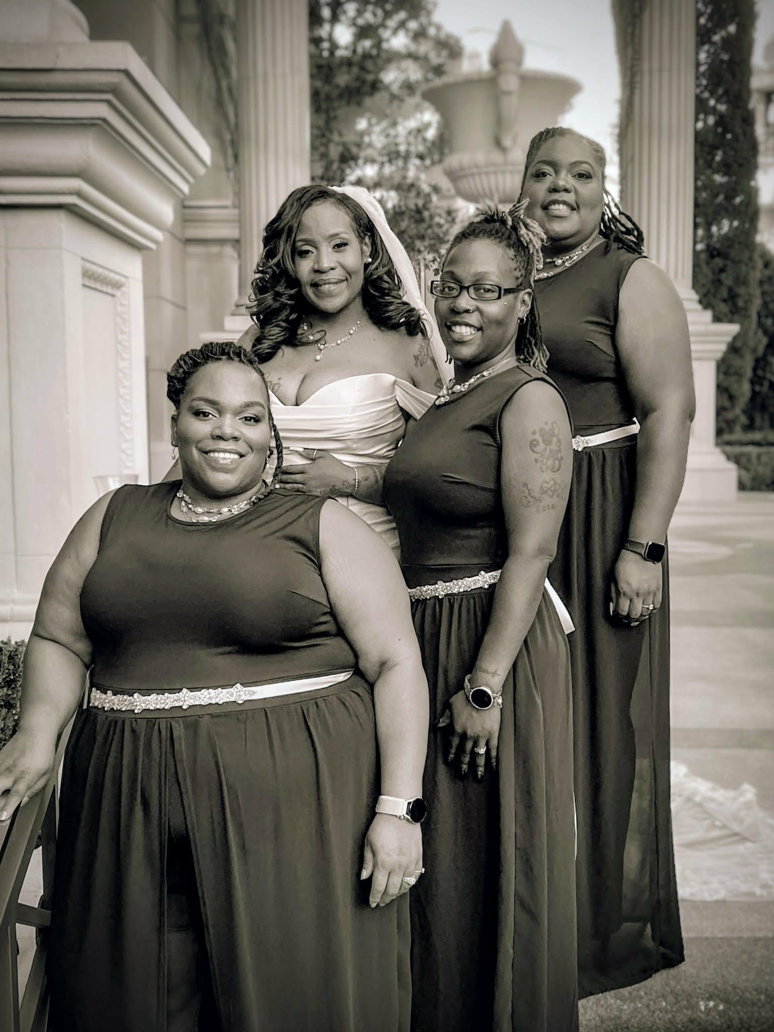 Four women in formal dresses posing together on a grand staircase outdoors