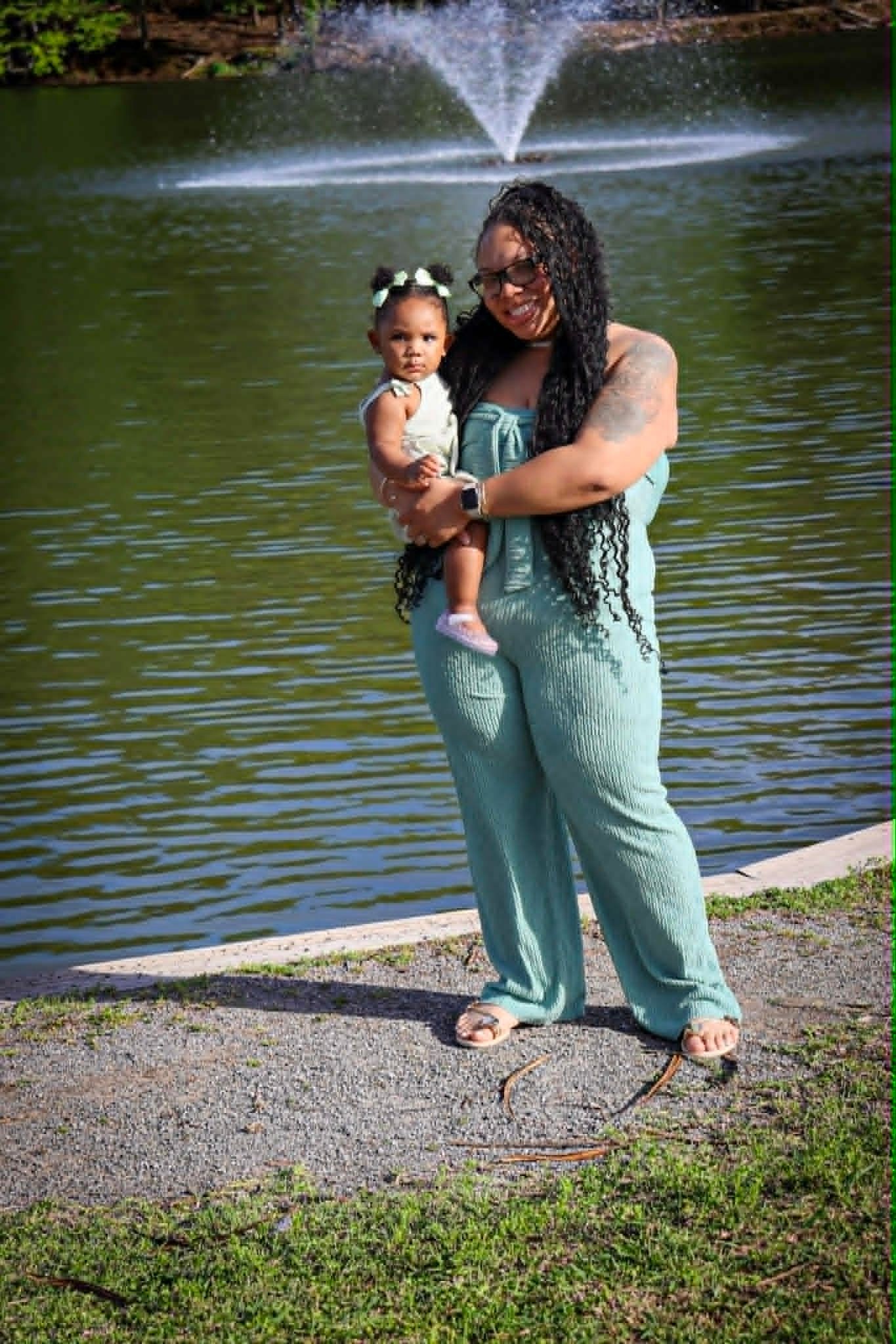 Person holding a child by a pond with a fountain in the background