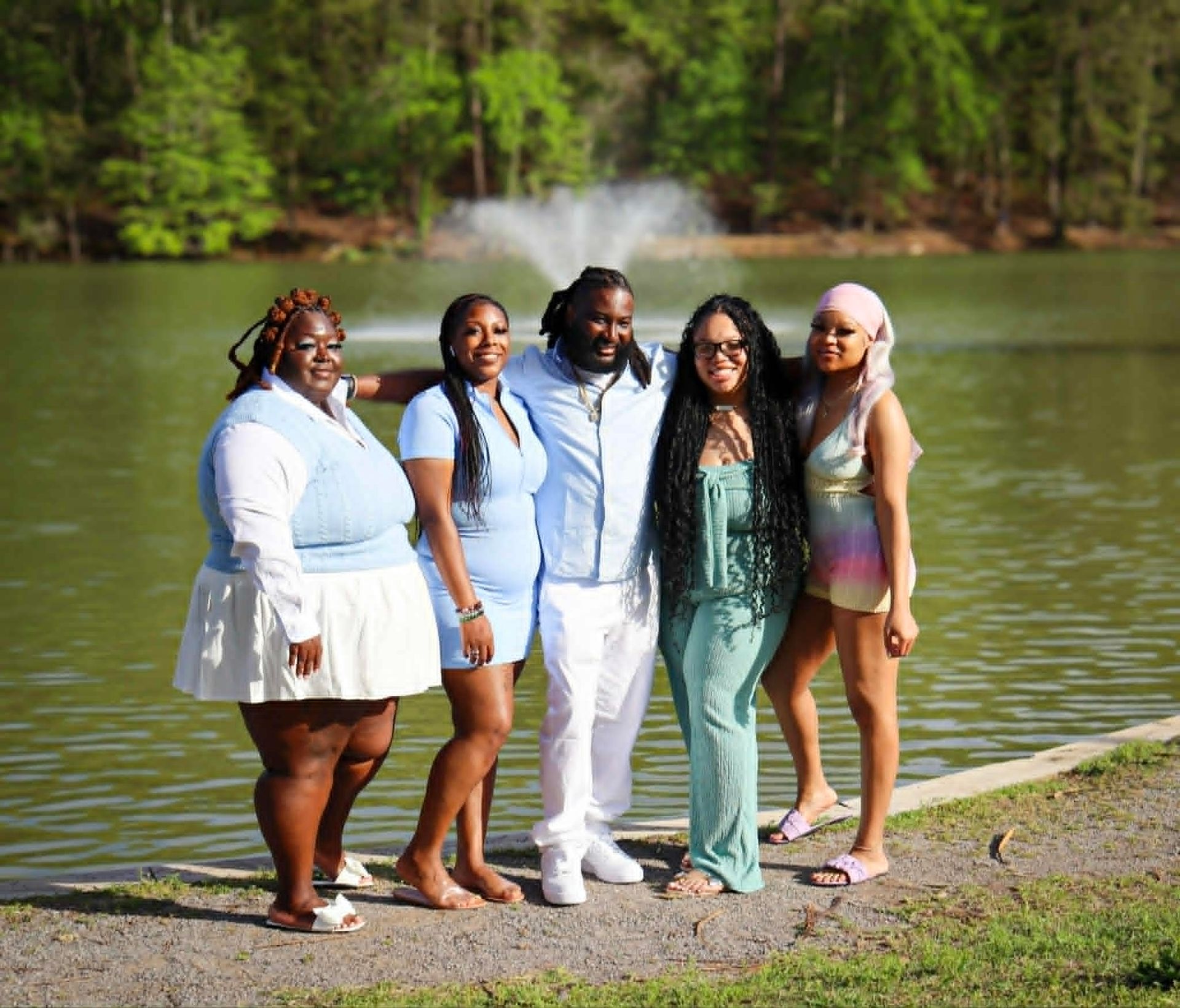 Five friends posing by a lake, with trees and a fountain in the background.