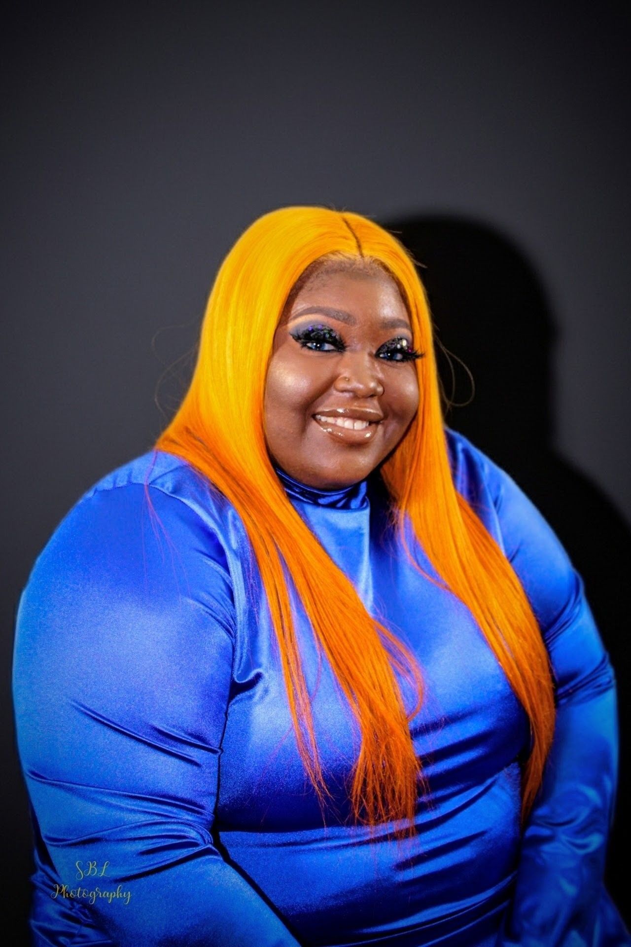 Smiling person in a bright blue top with long orange hair against a dark background