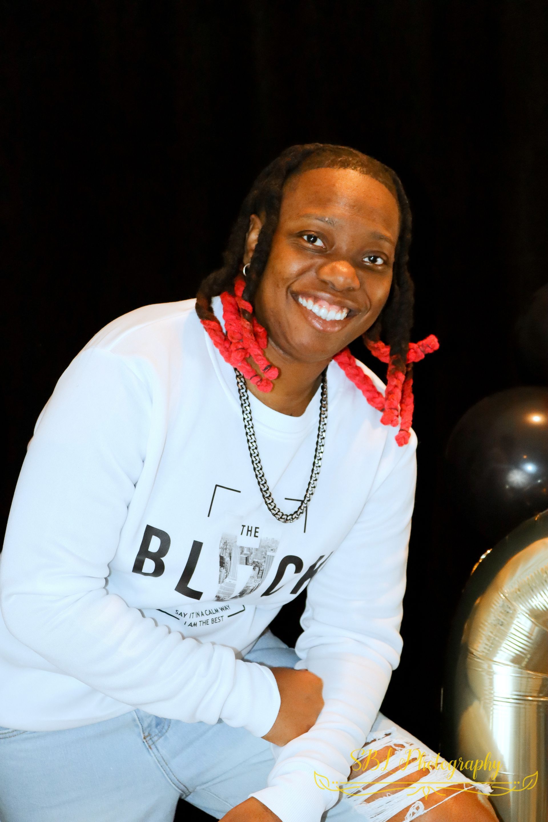 Smiling person in a white sweatshirt with red braids, seated against a black background