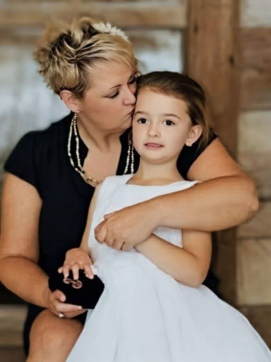 Woman hugging a young child in a white dress indoors