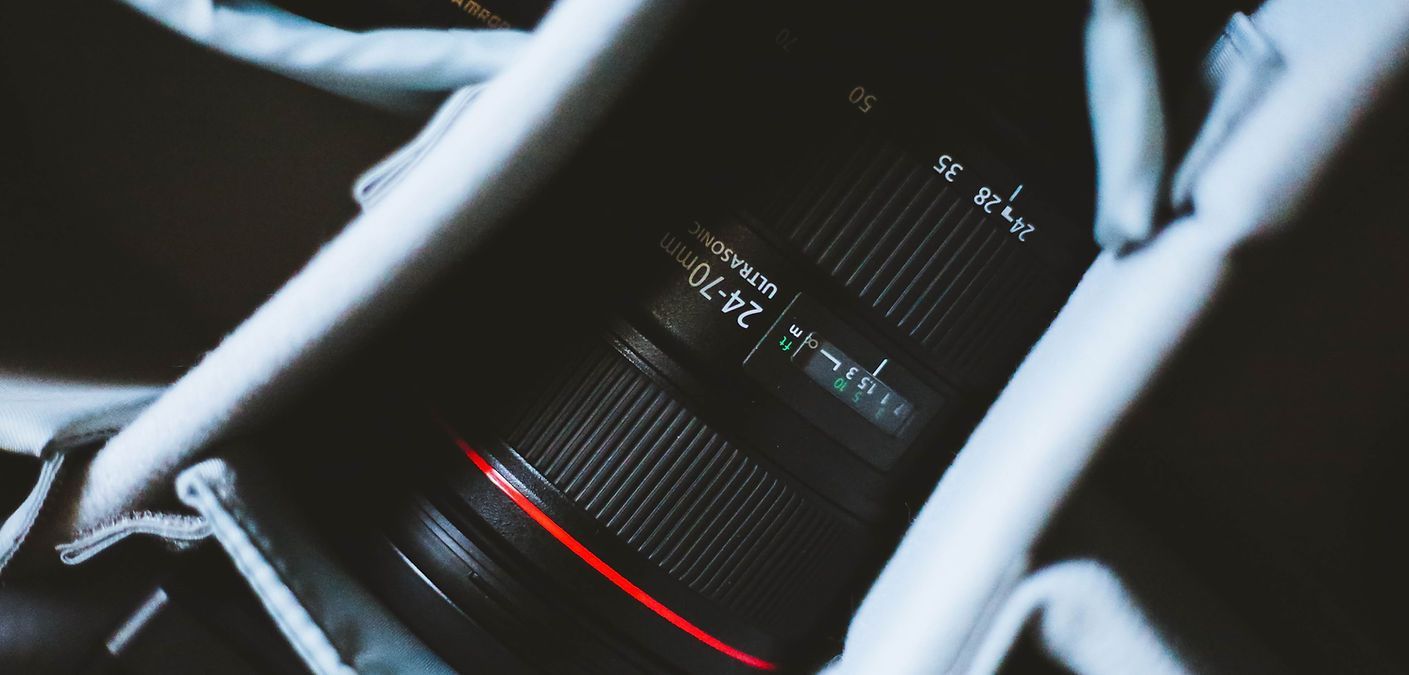 Close-up of a camera lens with red accent, framed by white rails in a dark setting