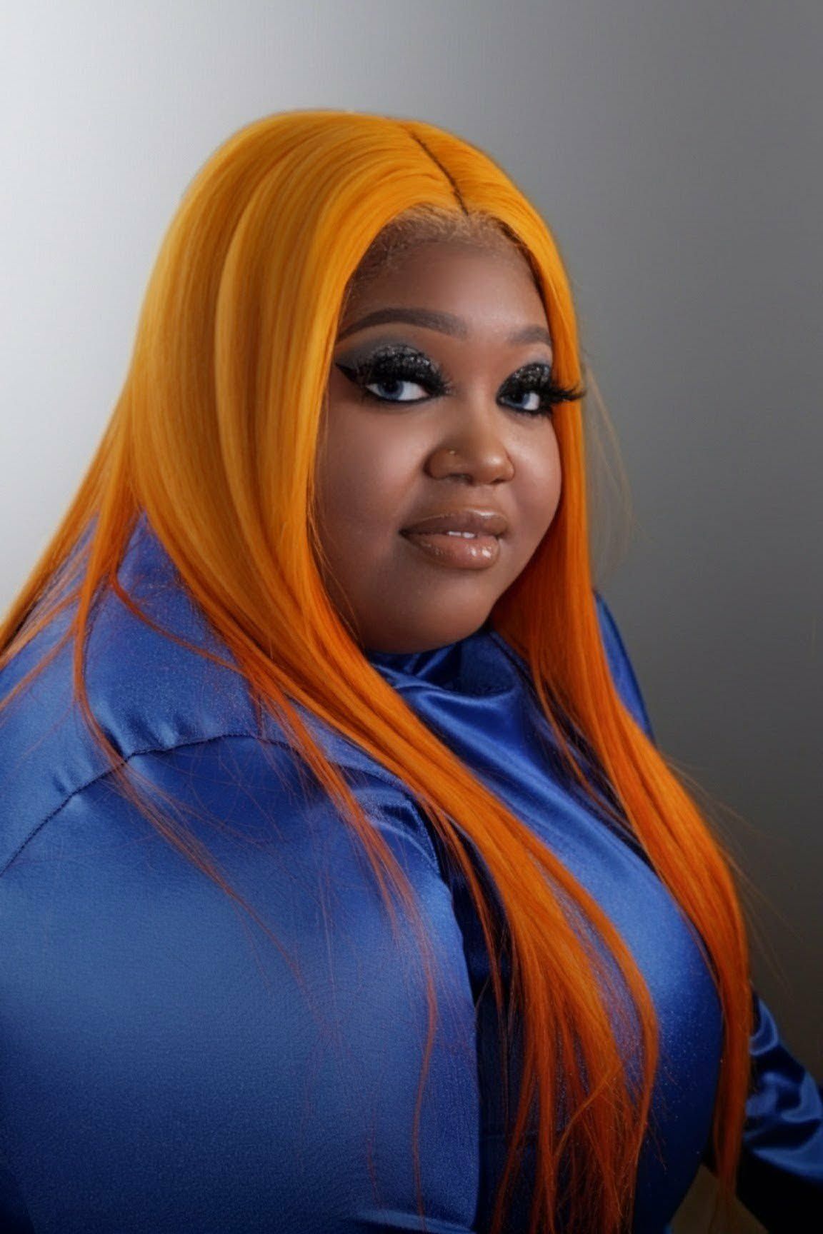 Portrait of a person with long orange hair in a blue outfit, posing against a gray background