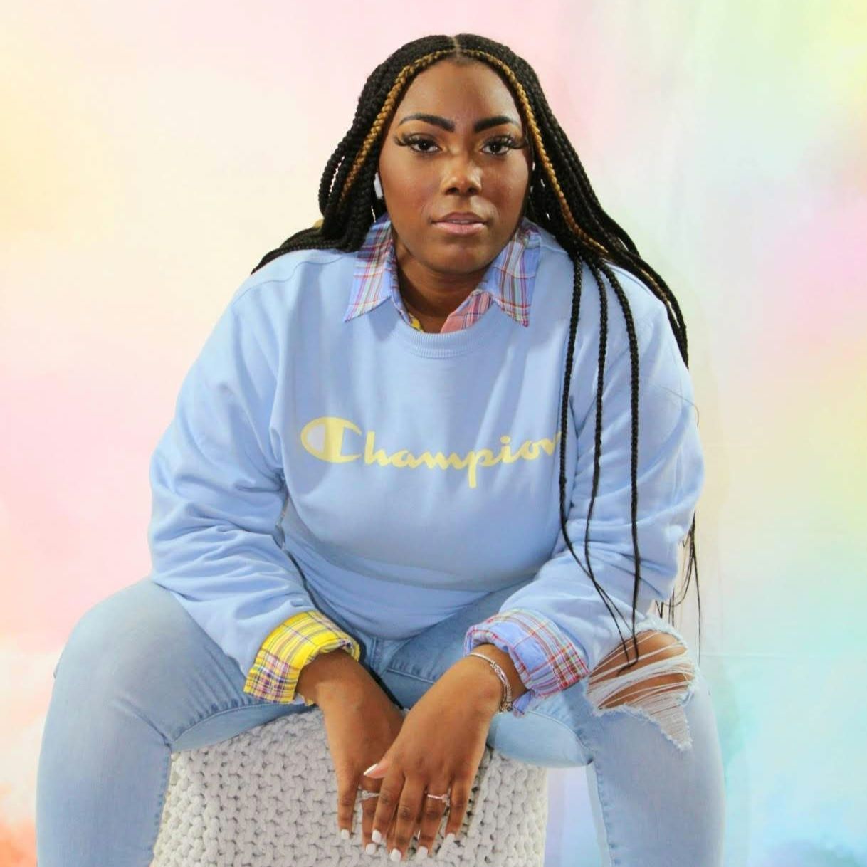 Person in a light blue Champion sweatshirt and jeans sits against a pastel gradient background.