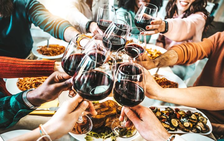 un gruppo di persone tiene in mano bicchieri di vino e brinda a un tavolo con cibo .