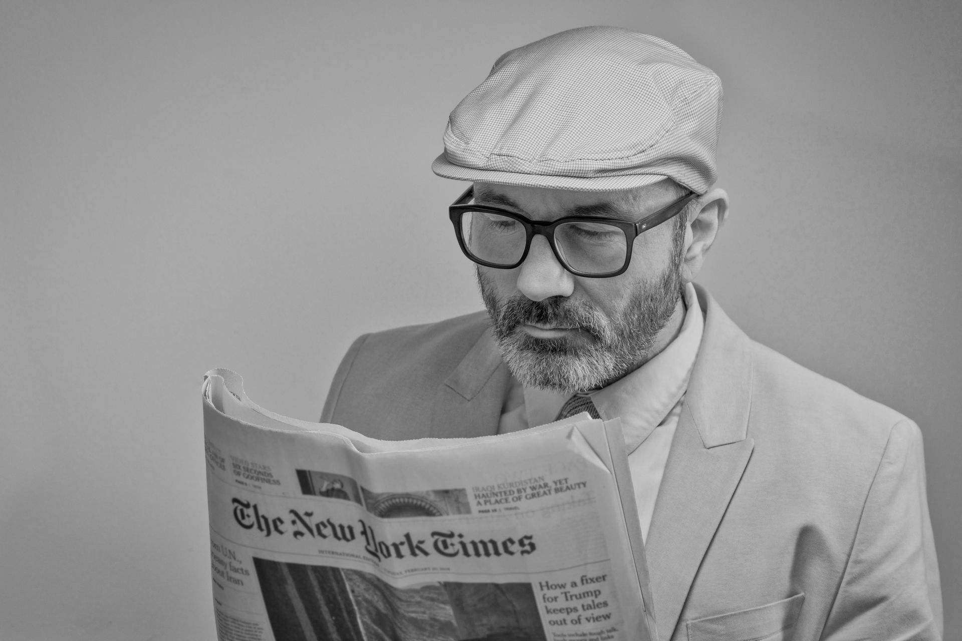 Een man met een bril, pet en colbert leest een krant in de New York Times.