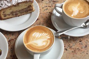 two cups of Latte Art served with a slice of tea cake