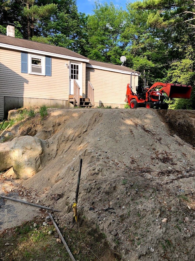 House with steep dirt slope and a red construction machine in the yard