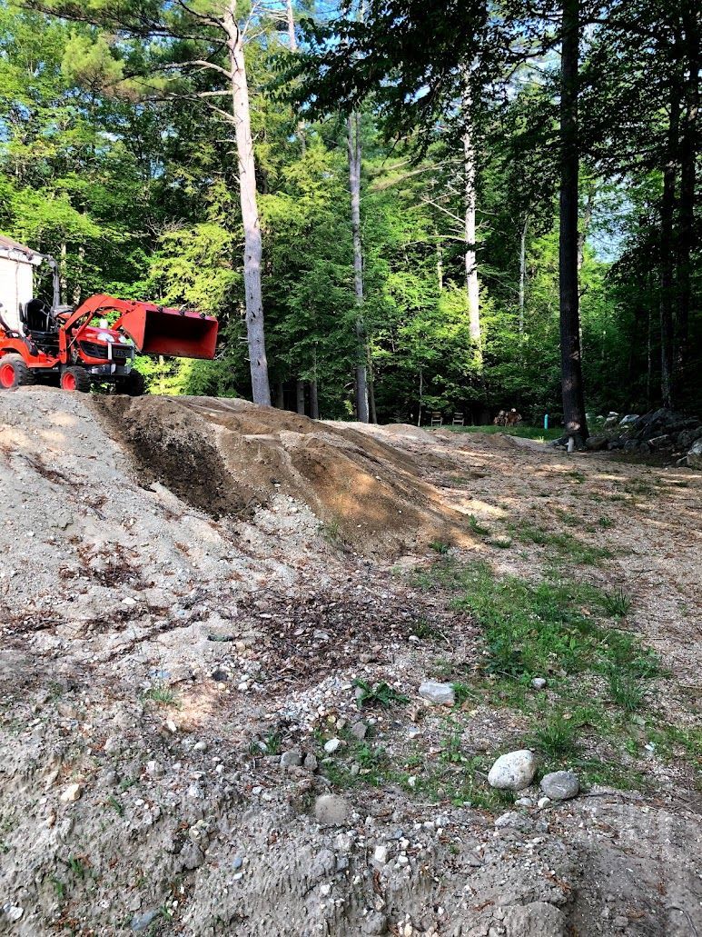 Red tractor on gravel pile in a wooded clearing with tall trees